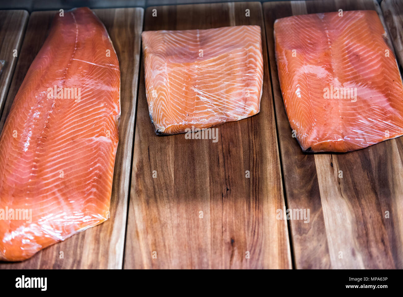 Large smoked raw salmon fillet cut on stand in seafood market shop store on display wrapped in plastic Stock Photo