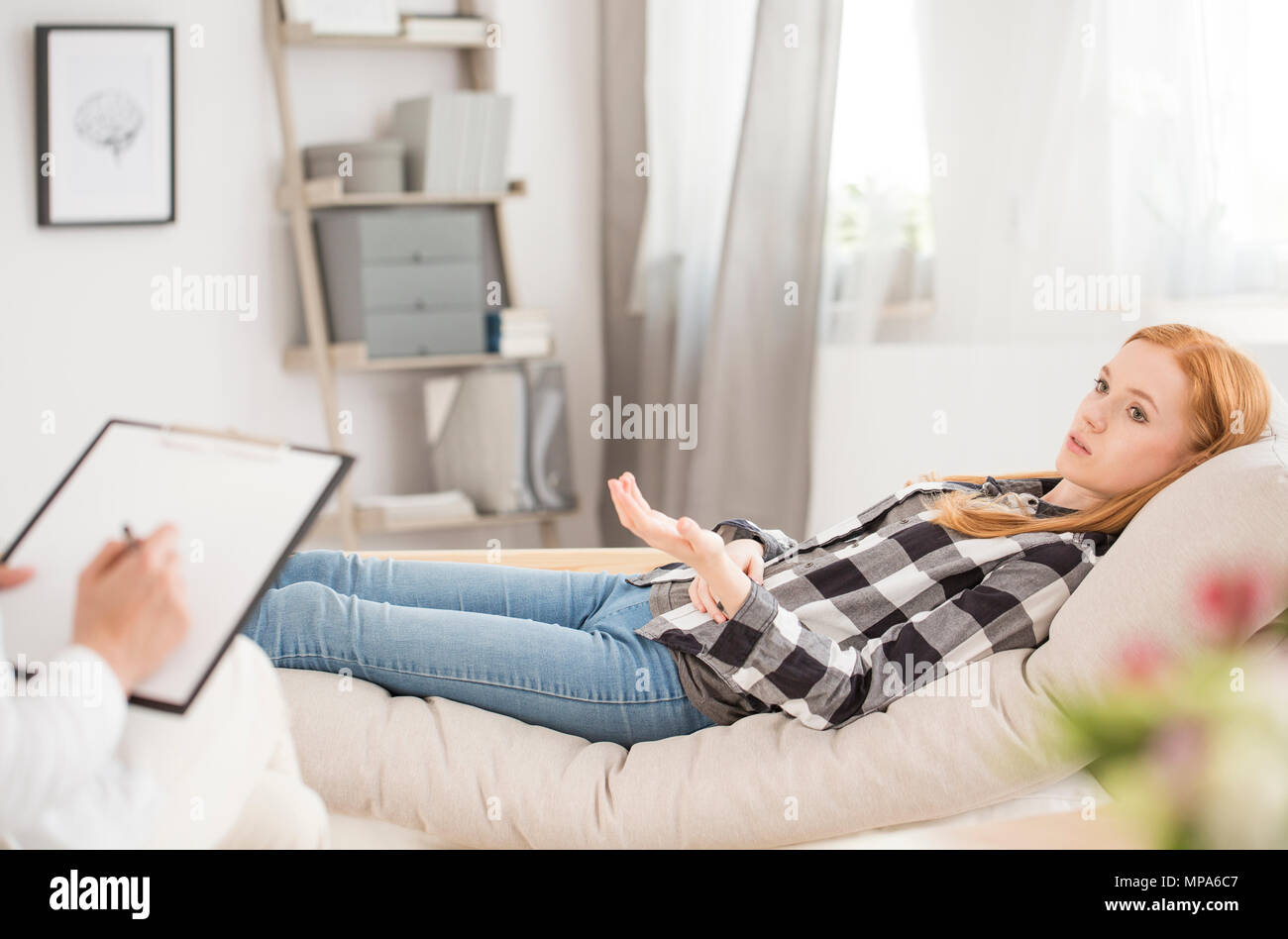 Young woman lying on couch at psychiatrist's office speaking about her personal emotional problems Stock Photo