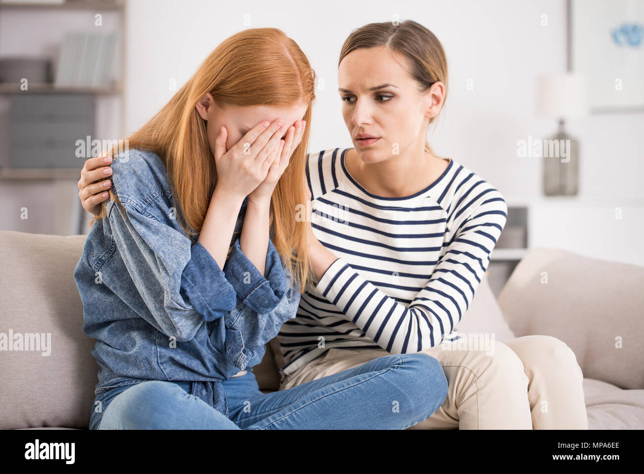 Young depressed woman crying being comforted by friend at home, girl being consoled by sister, mental problem and depression concept Stock Photo