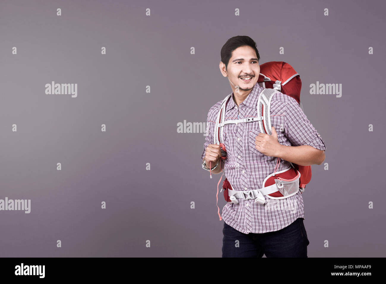 Happy asian backpacker ready to make a trip over colored background ...