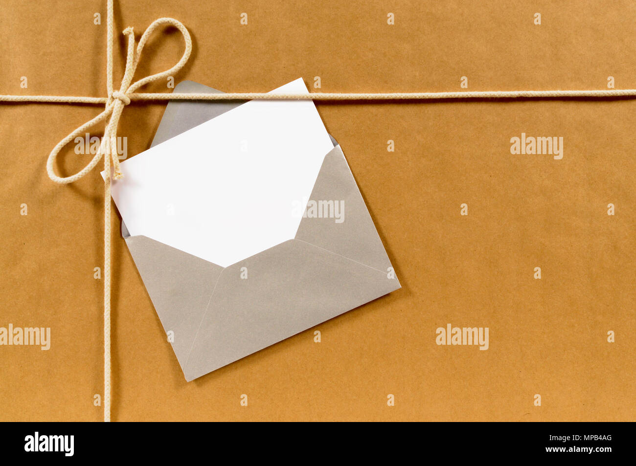 Brown paper parcel with silver envelope and blank message card Stock Photo Alamy