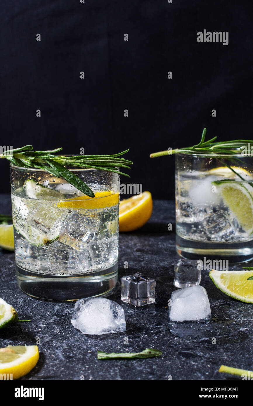 Alcoholic drink gin tonic cocktail with lemon, rosemary and ice on stone table. Stock Photo