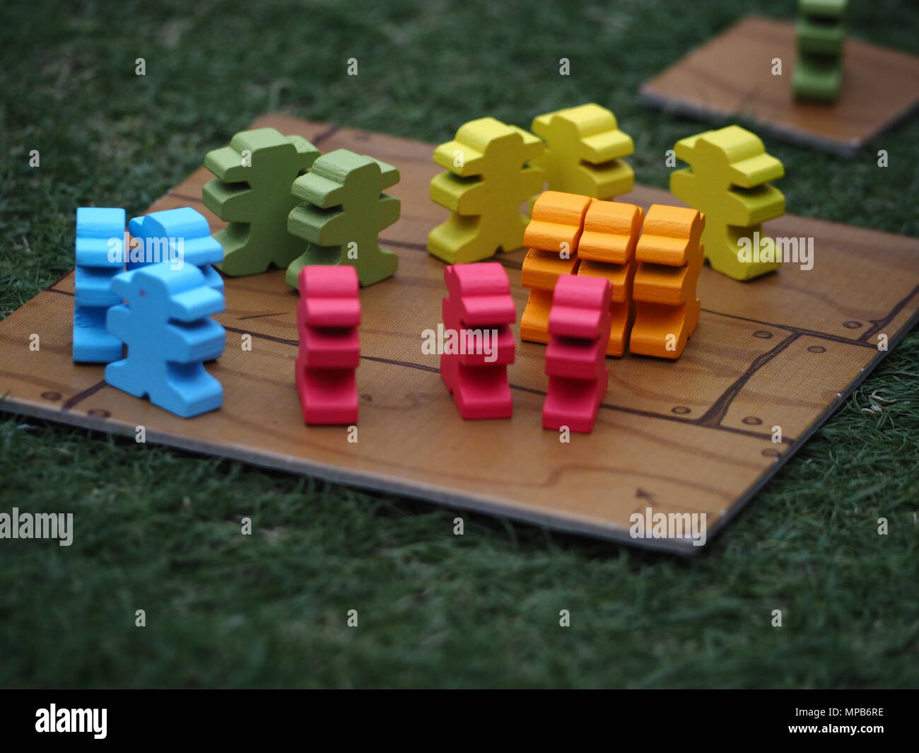 Multi-coloured pirate-themed board game pieces in the shape of men representing teams, on a wooden platform on grass. Stock Photo