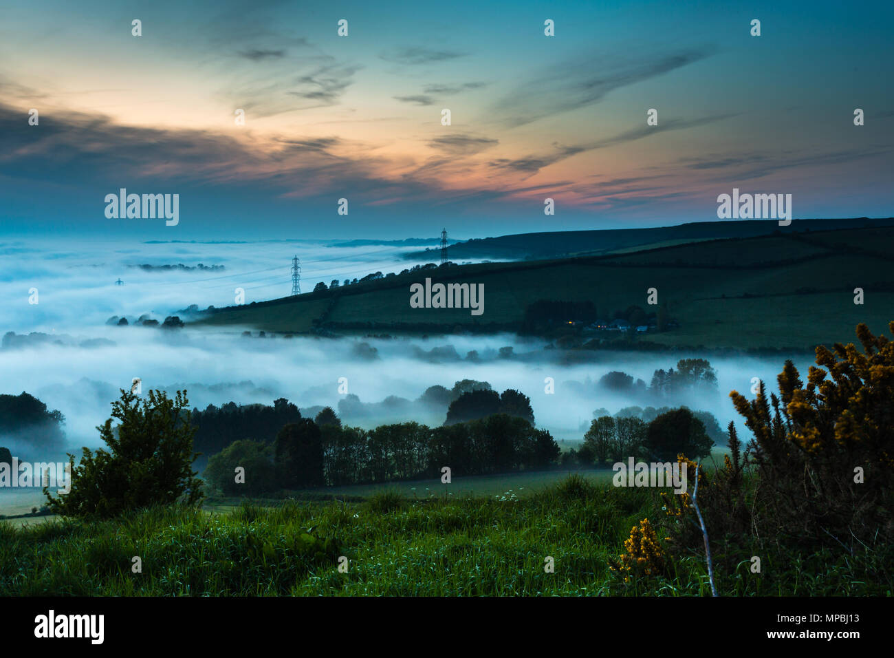 Dense, heavy, rolling, low lying evening cloud, fog or mist over Askerswell village, Dorset in English countryside at sunset viewed from hill by A35. Stock Photo