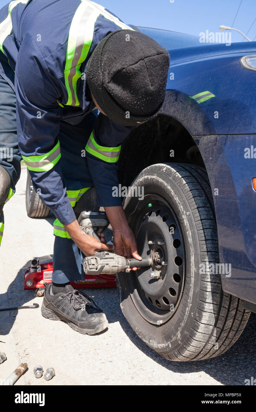 A service technician or person removing a flat tire or tyre using an impact wrench. Stock Photo