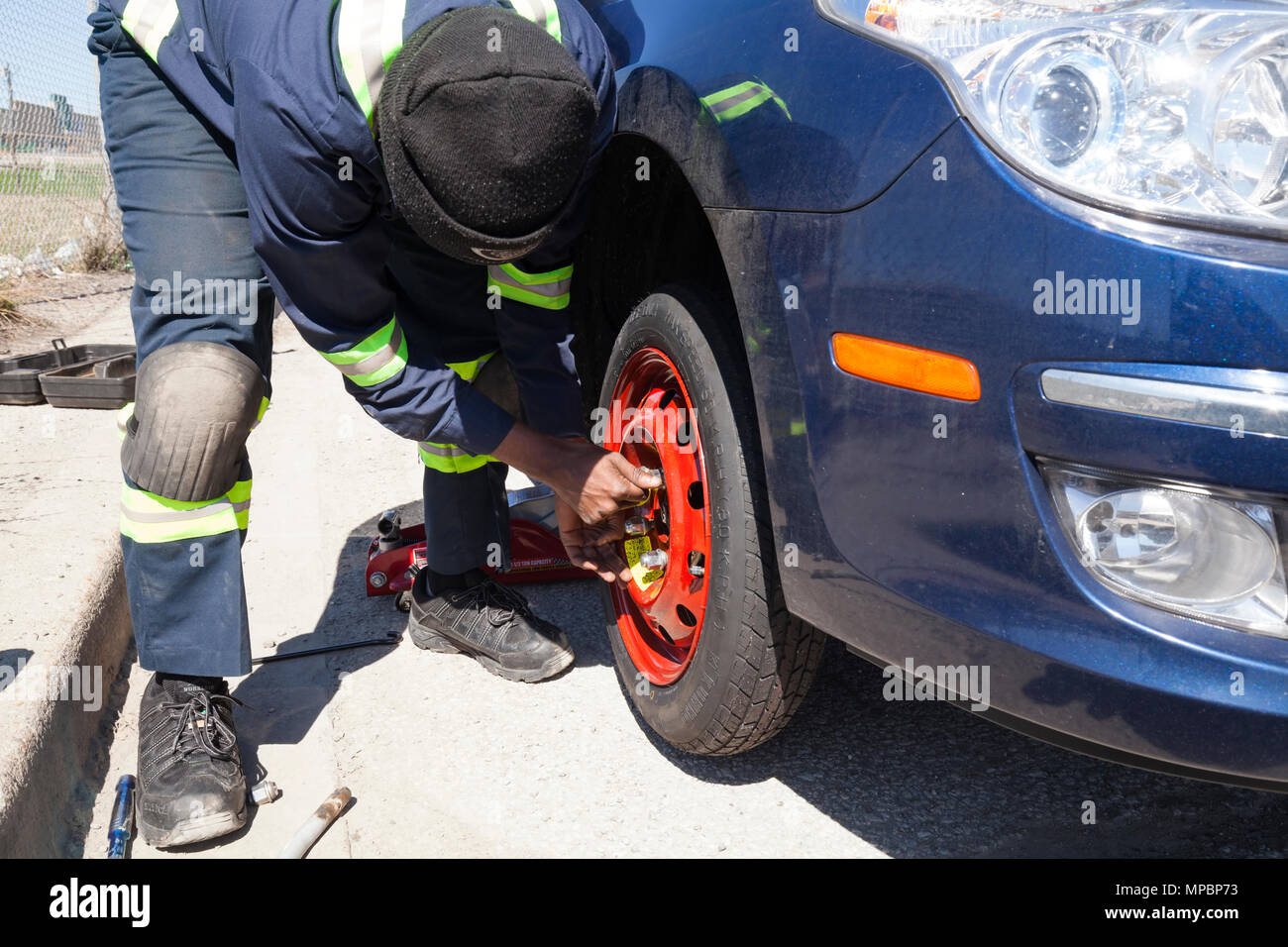 A service technician or person installing a spare tire or tyre. Stock Photo