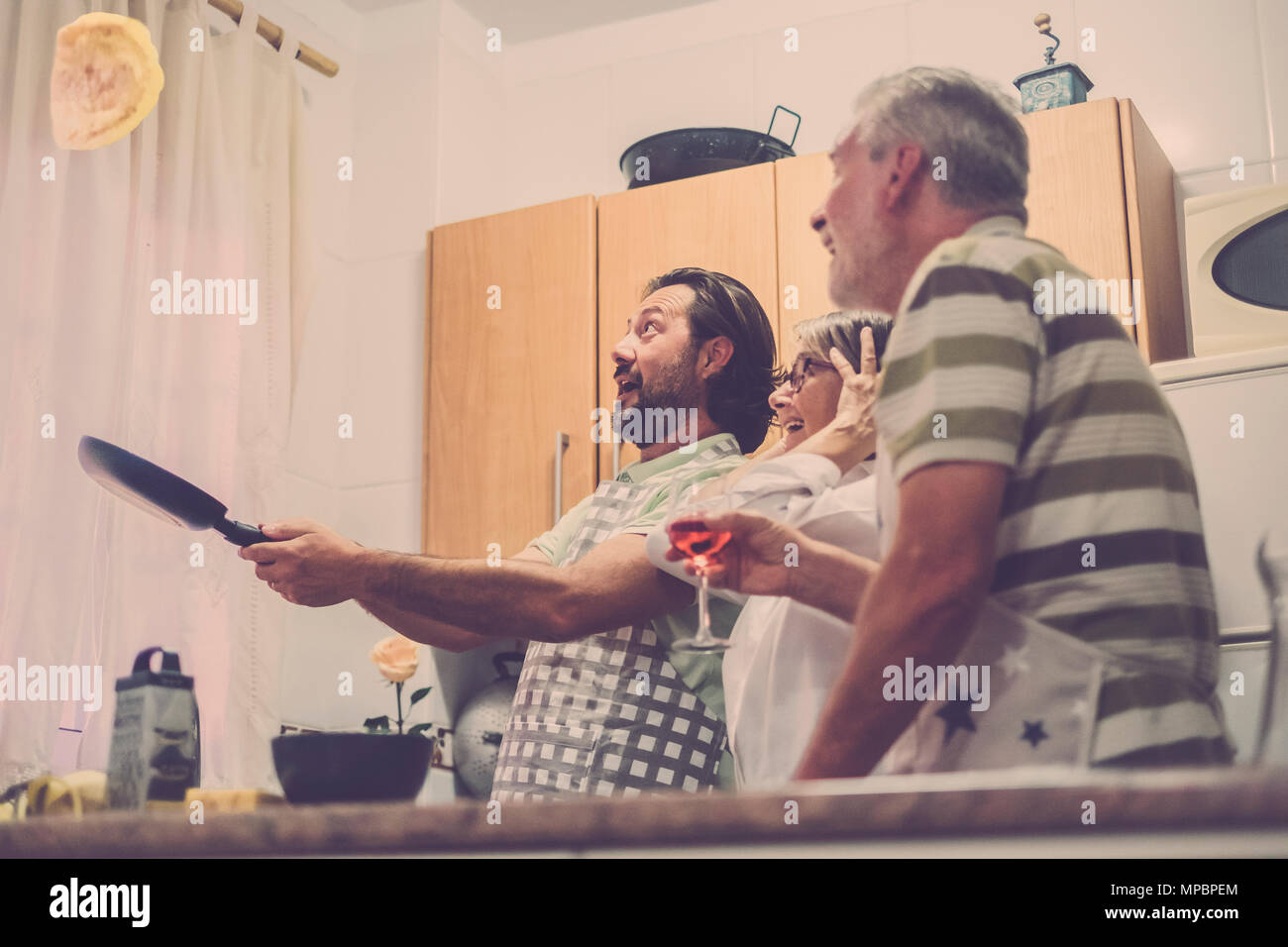 Flying eggs in the kitchen for a crazy and funny dinner prepared by three senior at home. Warm tones for family scene. Home food cook. Stock Photo