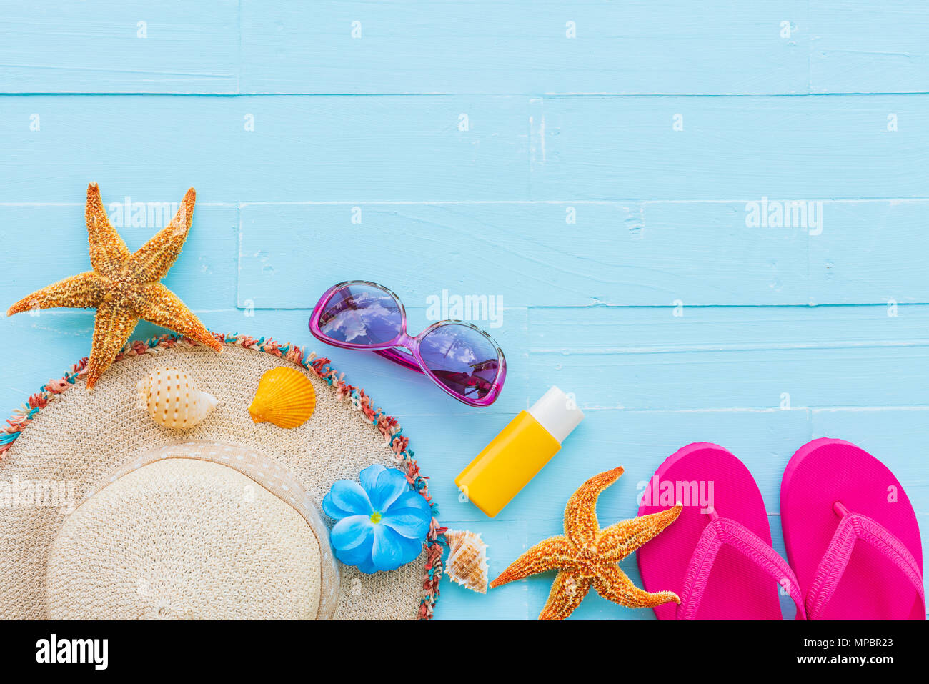 Beach accessories including sunglasses, starfish, hat beach, sunblock, colorful flip flop and shell on bright blue pastel wooden background for summer Stock Photo