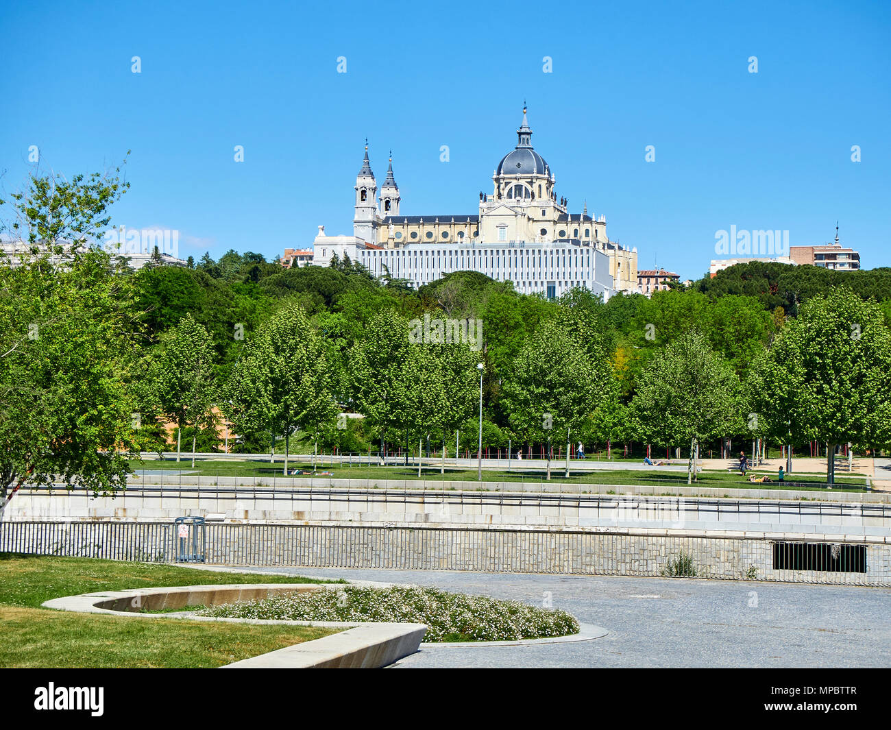 People enjoying a spring day in the Green spaces of Madrid Rio with the Almudena Cathedral in background. Madrid, Spain. Stock Photo