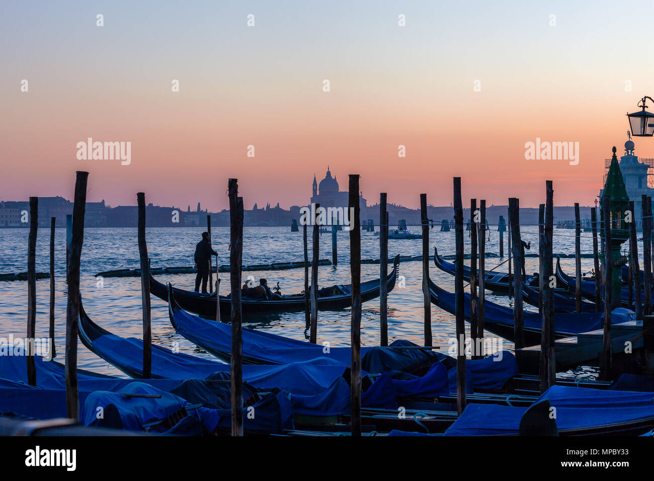 VENICE, ITALY - JANUARY 02 2018: Gondoloas  in the San Marco basin with Santissimo Redentore church and Giudecca island silhouette at sunset Stock Photo