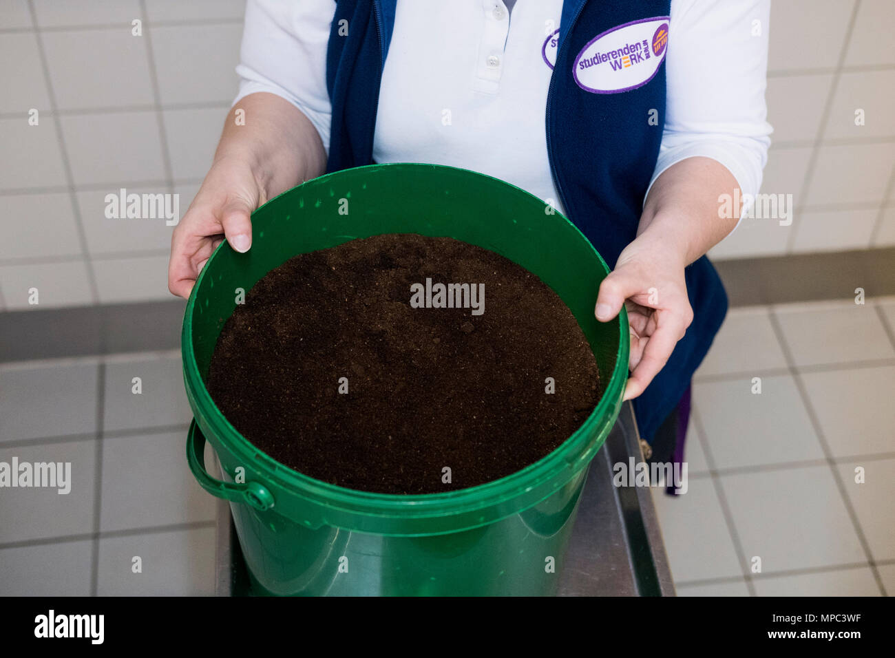 18 May 2018, Germany, Berlin: Melanie Potalivo, employee of the Technical University (TU) Berlin, holding a bucket with coffee grounds, which is collected at the canteen and kept for people to pick up themselves. The demand for fertiliser is increasing with the begin of the gardening season among Berlin's balcony gardeners and allotment holders. They are able to collect coffee grounds as fertiliser free of charge at Berlin universities. Photo: Kristin Bethge/dpa Stock Photo