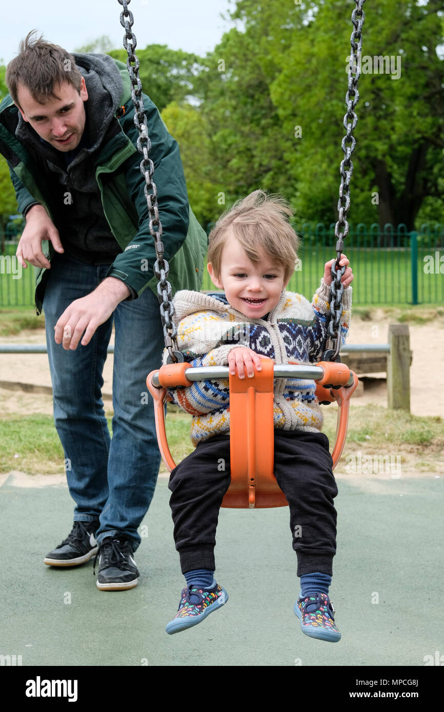 Father pushing his 18 month old son on a playground swing Stock Photo