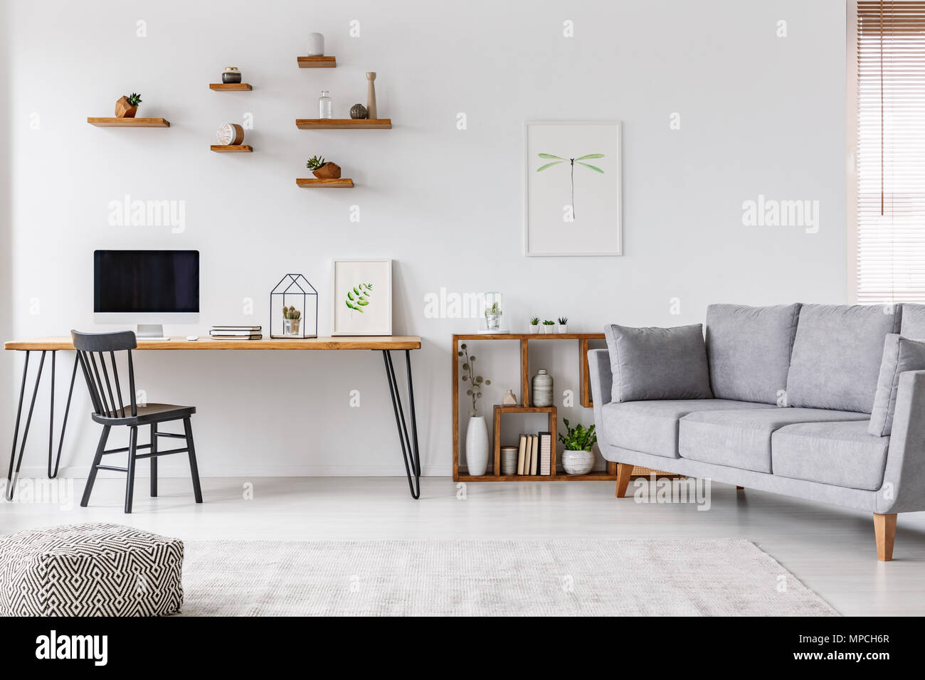 Grey sofa near black chair at desk with computer monitor in open space interior with poster. Real photo Stock Photo