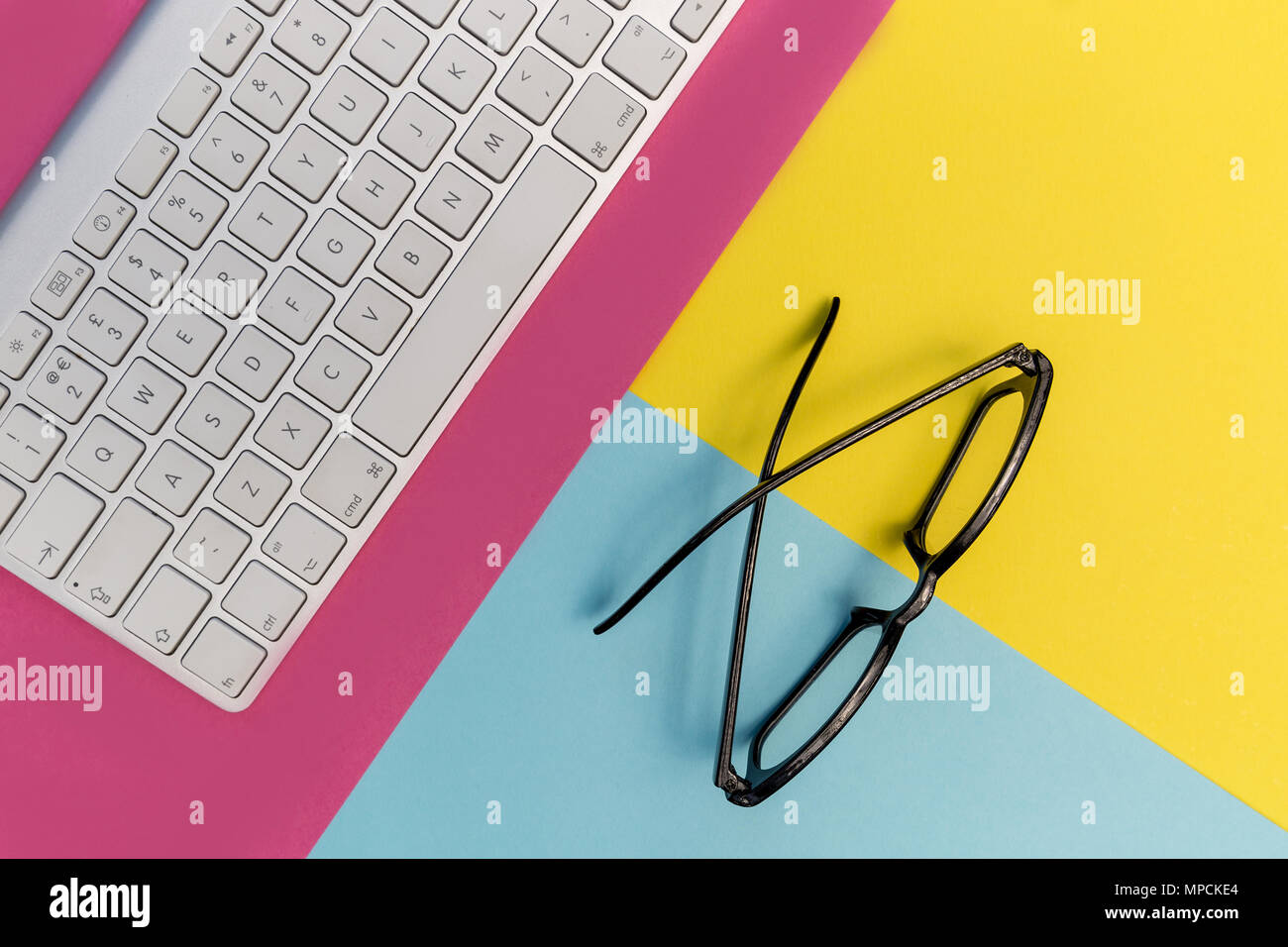 Computer keyboard eyeglasses on bright pink yellow background Stock Photo