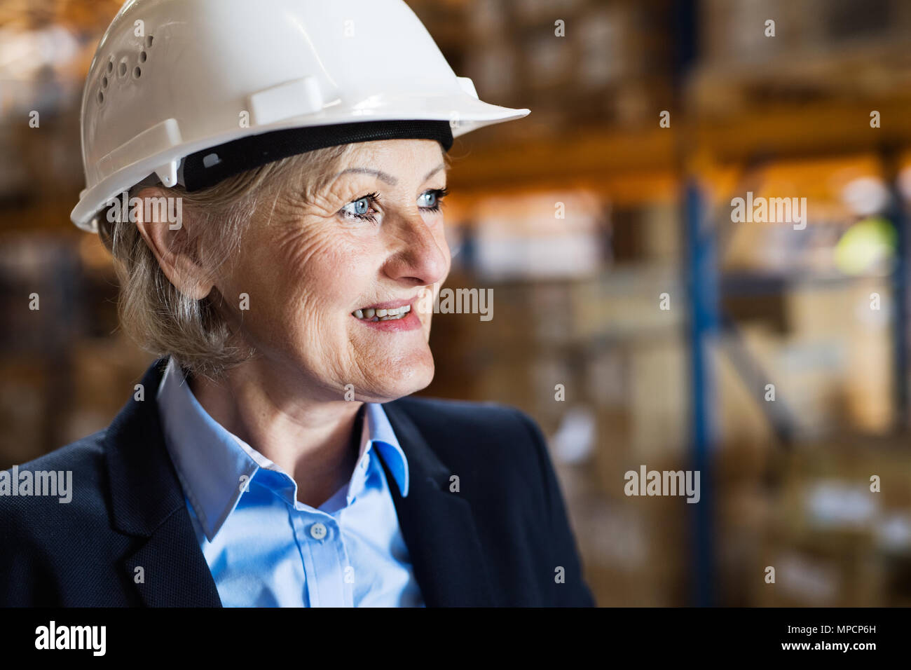 Senior woman warehouse manager or supervisor with white helmet. Stock Photo