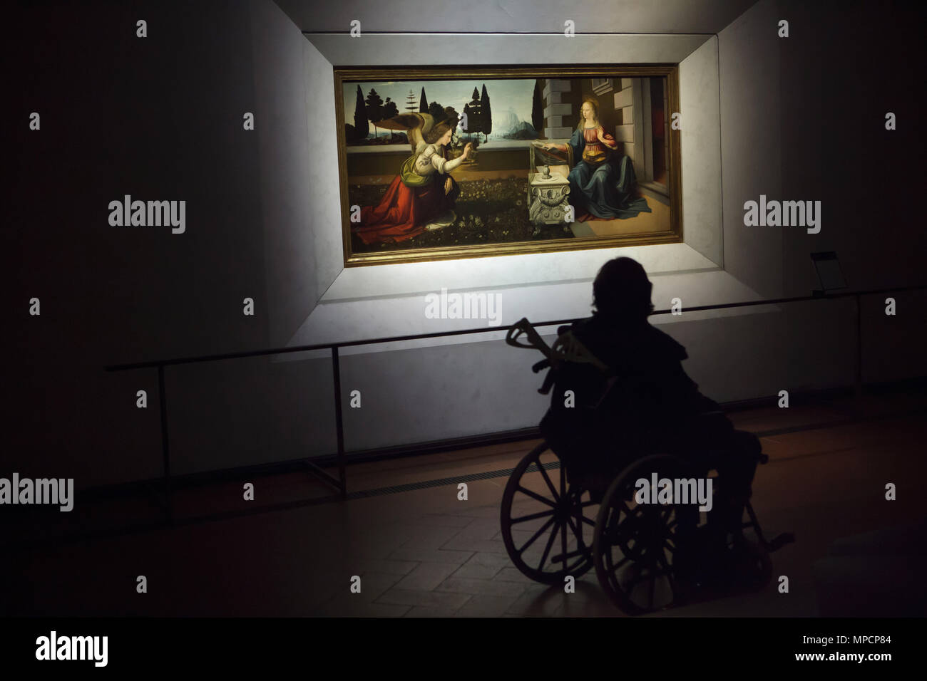 Disabled person in the wheelchair in front of the painting Annunciation (1472–1475) by Italian Renaissance painter Leonardo da Vinci displayed in the Uffizi Gallery (Galleria degli Uffizi) in Florence, Tuscany, Italy. Stock Photo