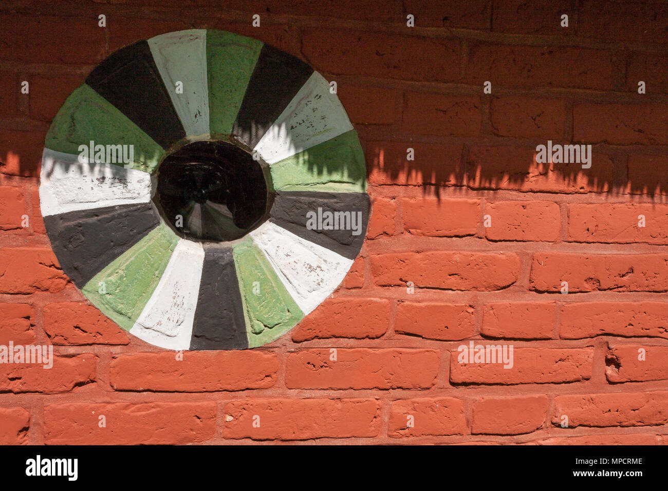 Window in a Danish red brick barn: Detail of the wall of an old barn in the Lyngby Folk museum.  A round window decorated with green, white and black paint shaded by the thatched roof. Stock Photo