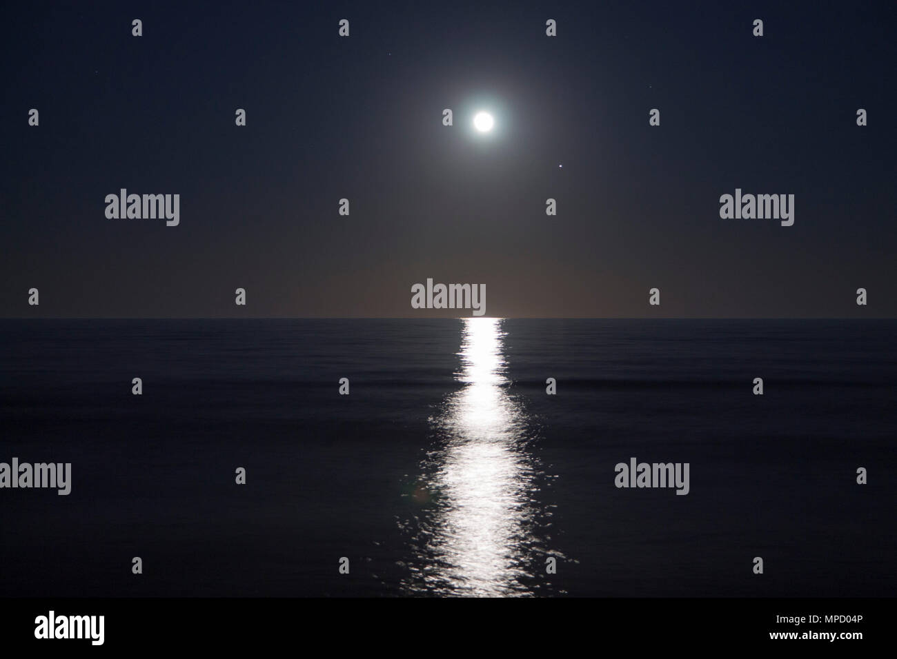 Big full moon is rising above the sea at night. Lunar light reflected on the water. Lunar path and ocean. Stock Photo