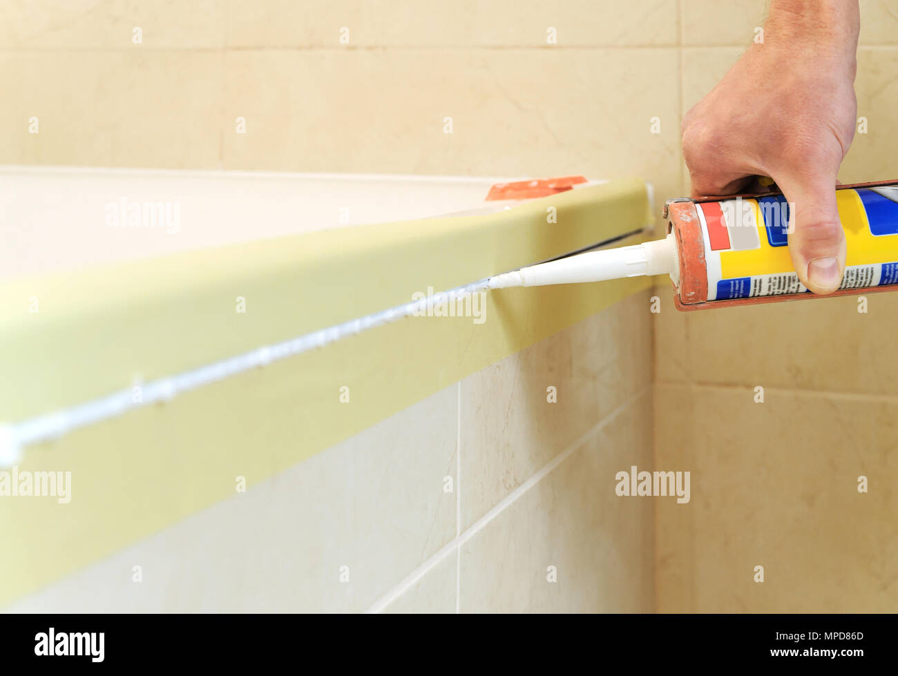 Worker puts silicone sealant to caulk the joint between tub and wall