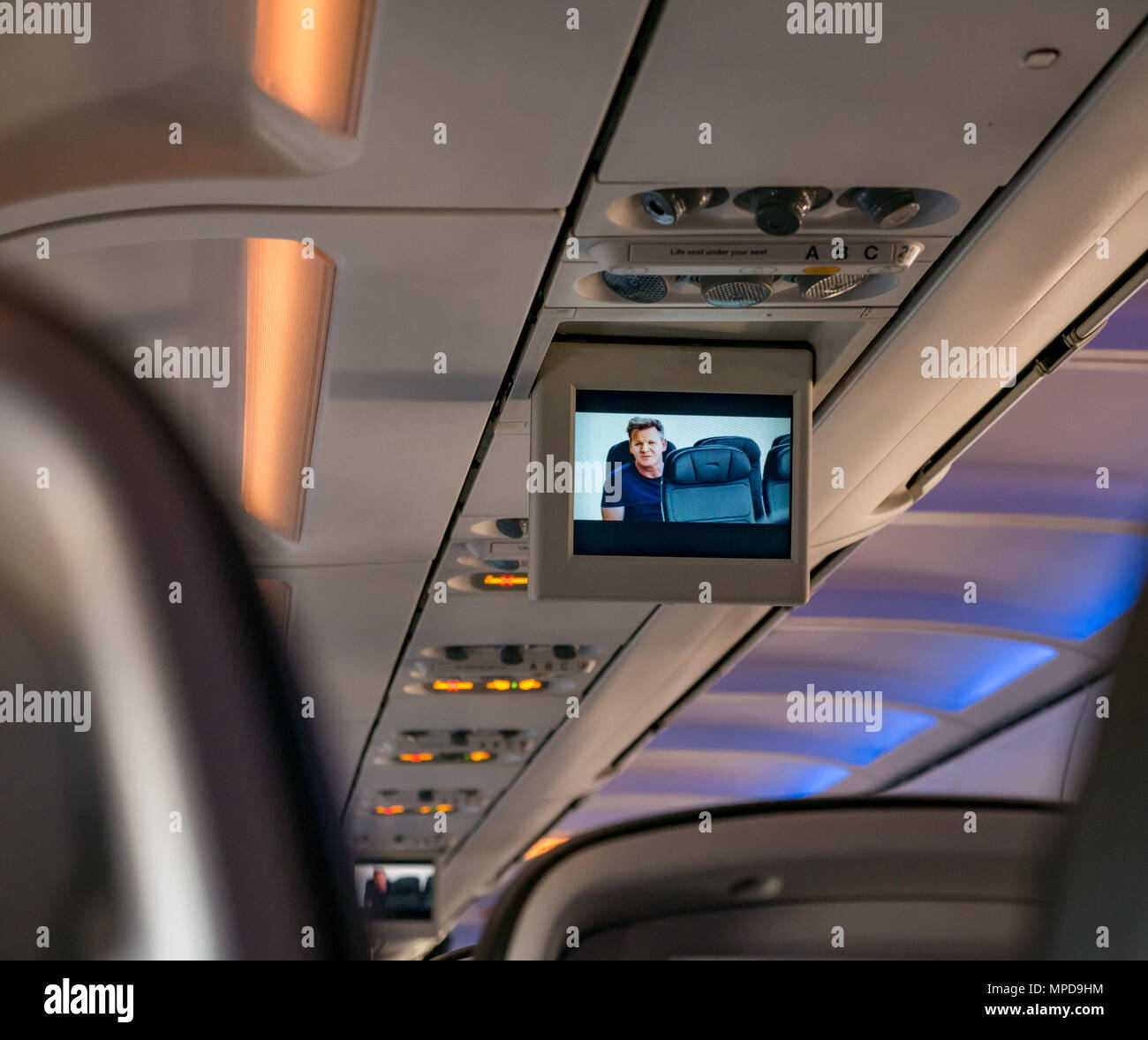 View from British Airways airline seat down plane cabin with safety video featuring Gordon Ramsey Stock Photo