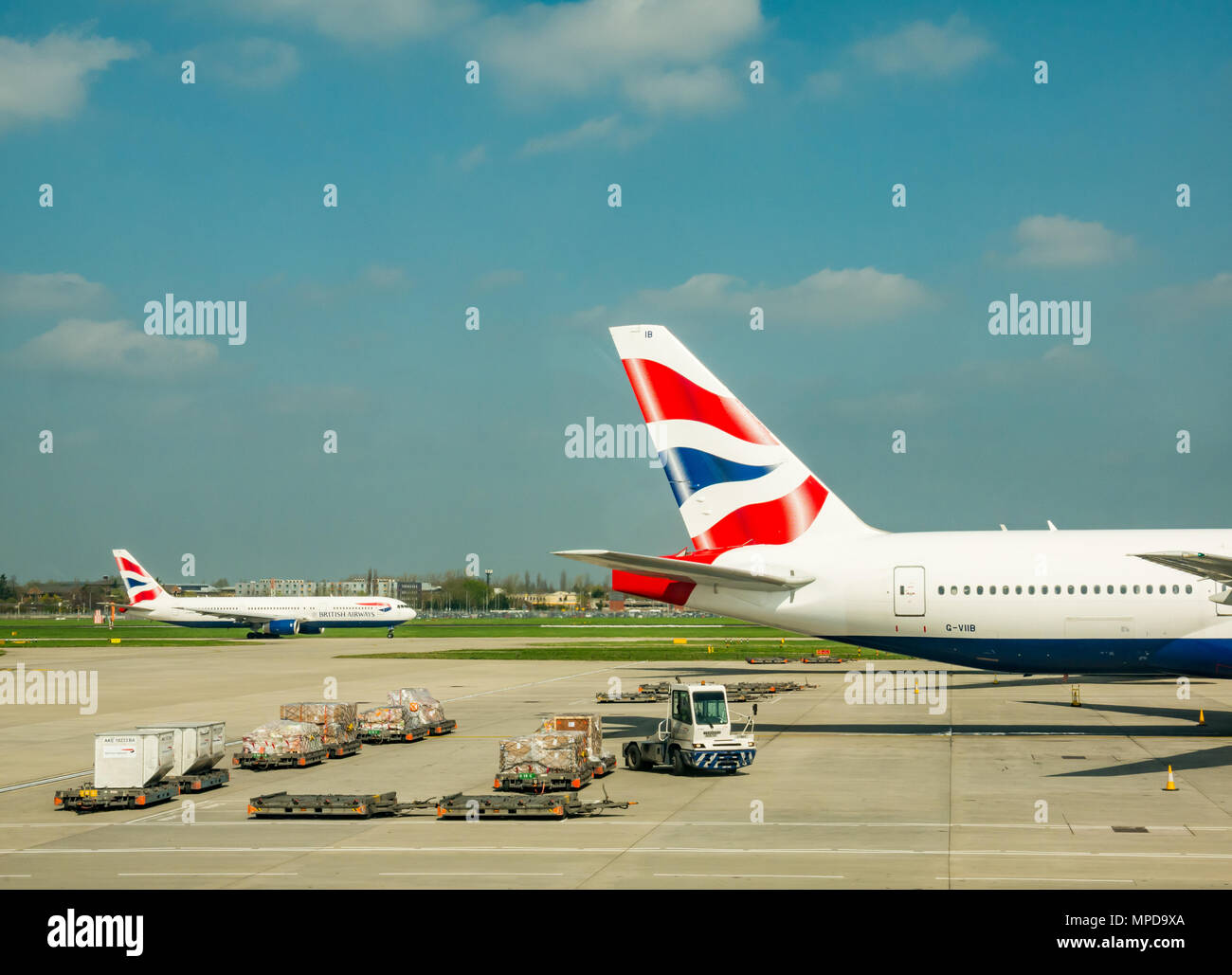 British Airways planes, including a Boeing 777 on airport apron with airport vehicles, Terminal 5, Heathrow airport, London, England, UK Stock Photo