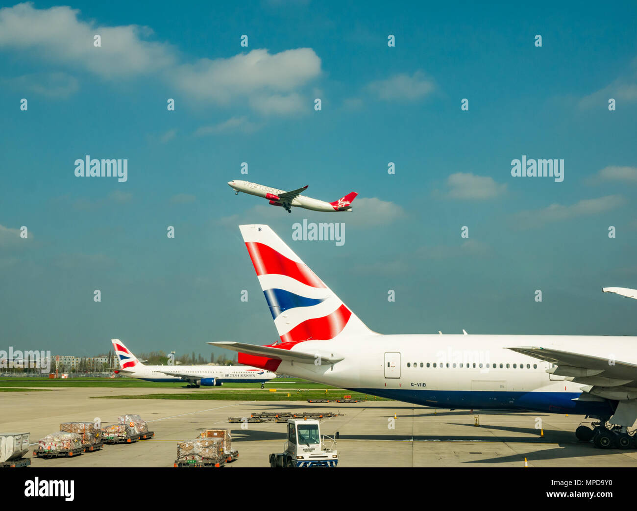 British Airways Boeing 777 on airport apron, Virgin Atlantic aeroplane taking off in blue sky, Terminal 5, Heathrow airport, London, England, UK Stock Photo