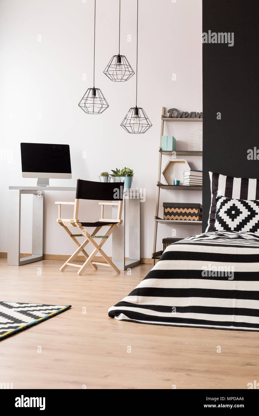 Black and white home interior with bed, pendant lamp, chair, desk and