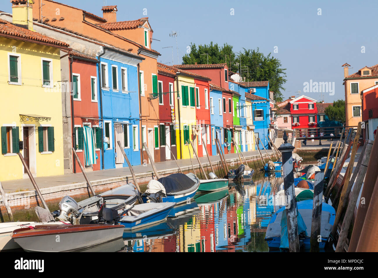 Brightly coloured fishermen's cottages reflected in a canal, Burano, Venice, Italy in early morning light. The island is a popular tourist attraction Stock Photo
