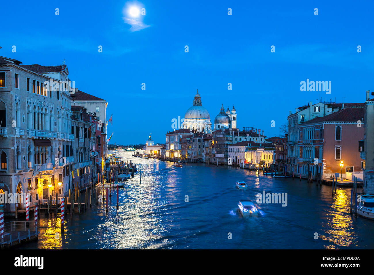 Full moon at blue hour over the Grand Canal, Venice, Veneto, Italy with Basilica di Santa Maria della Salute. Reflection on the water and a water taxi Stock Photo