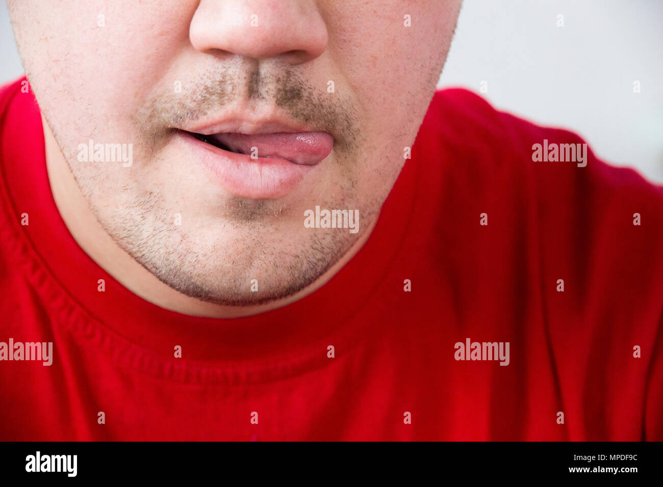 Unshaven man in red shirt tongue licking lips Stock Photo