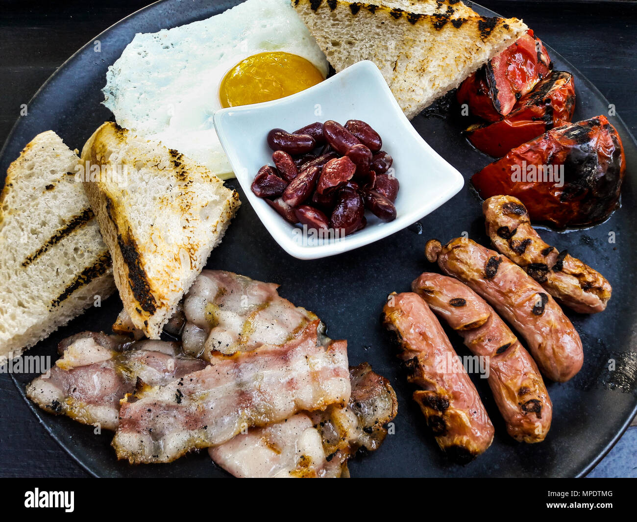 English Breakfast with Bacon, Red Beans, Sausage, Egg and Fried Bread on black surface. Stock Photo