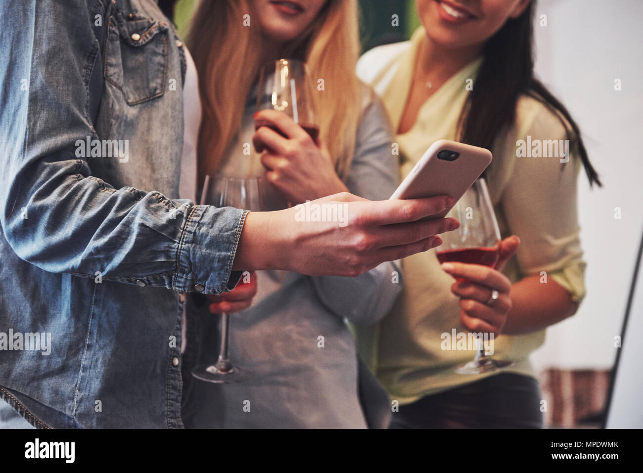 Picture presenting a happy group of girl friends with red wine. Together they see a photo on a smartphone Stock Photo