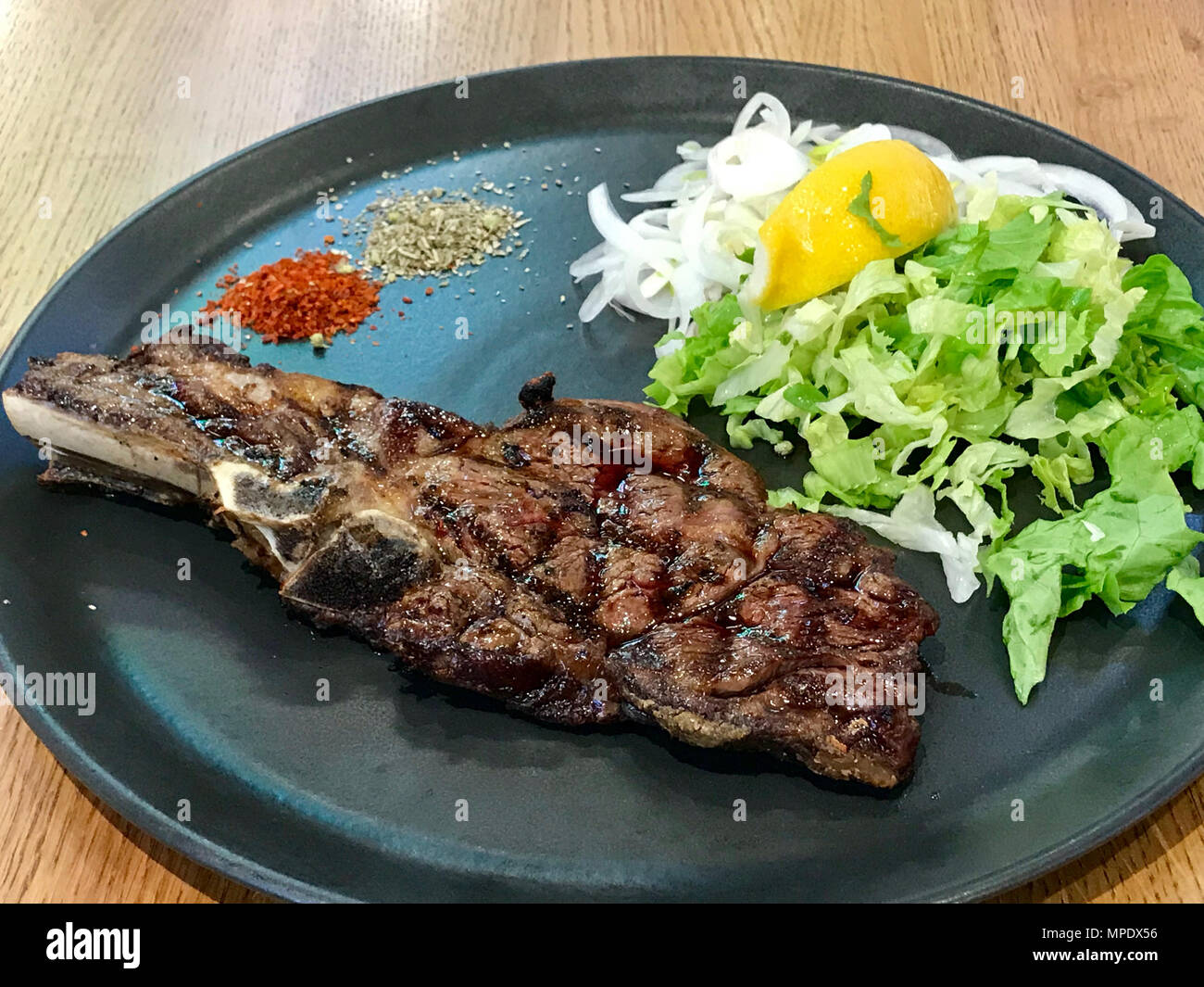 Big Veal Chop Steak with Salad served in Black Plate. Organic Food. Stock Photo