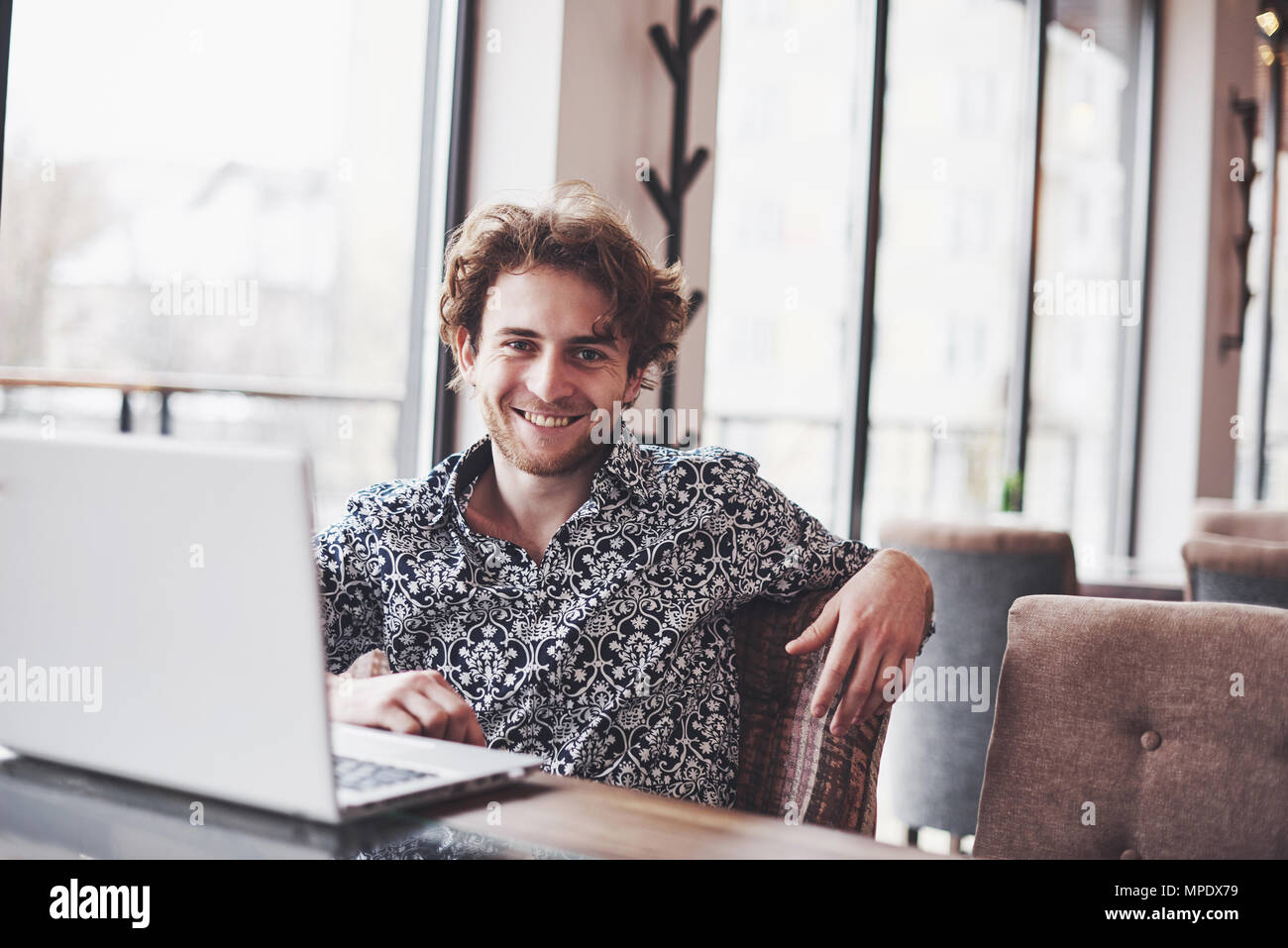 Young handsome man sitting in office with cup of coffee and working on project connected with modern cyber technologies. Businessman with notebook trying to keep deadline in digital marketing sphere Stock Photo