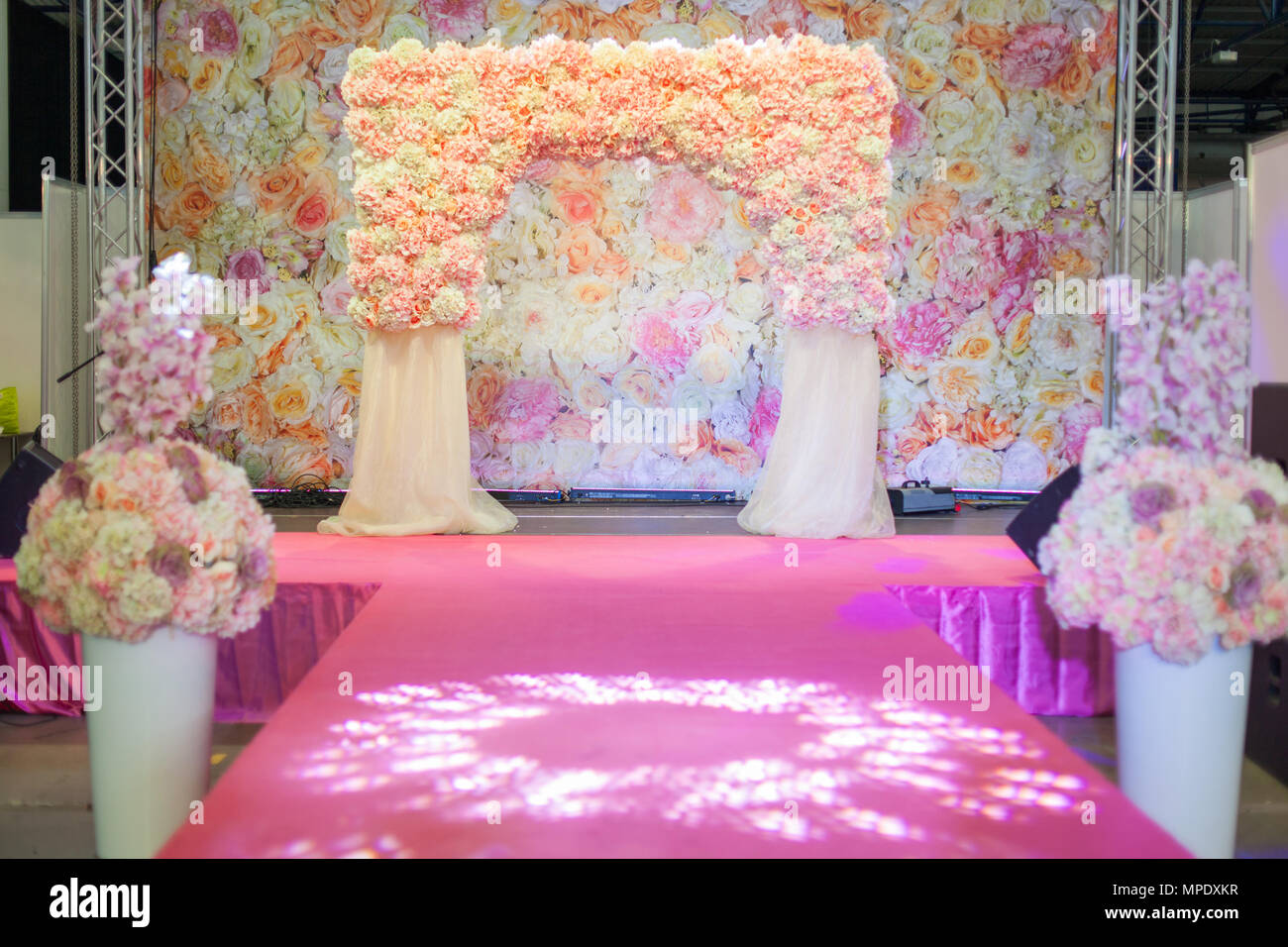 Wedding arch on the podium. Vases with flowers stand along the catwalk. Stock Photo
