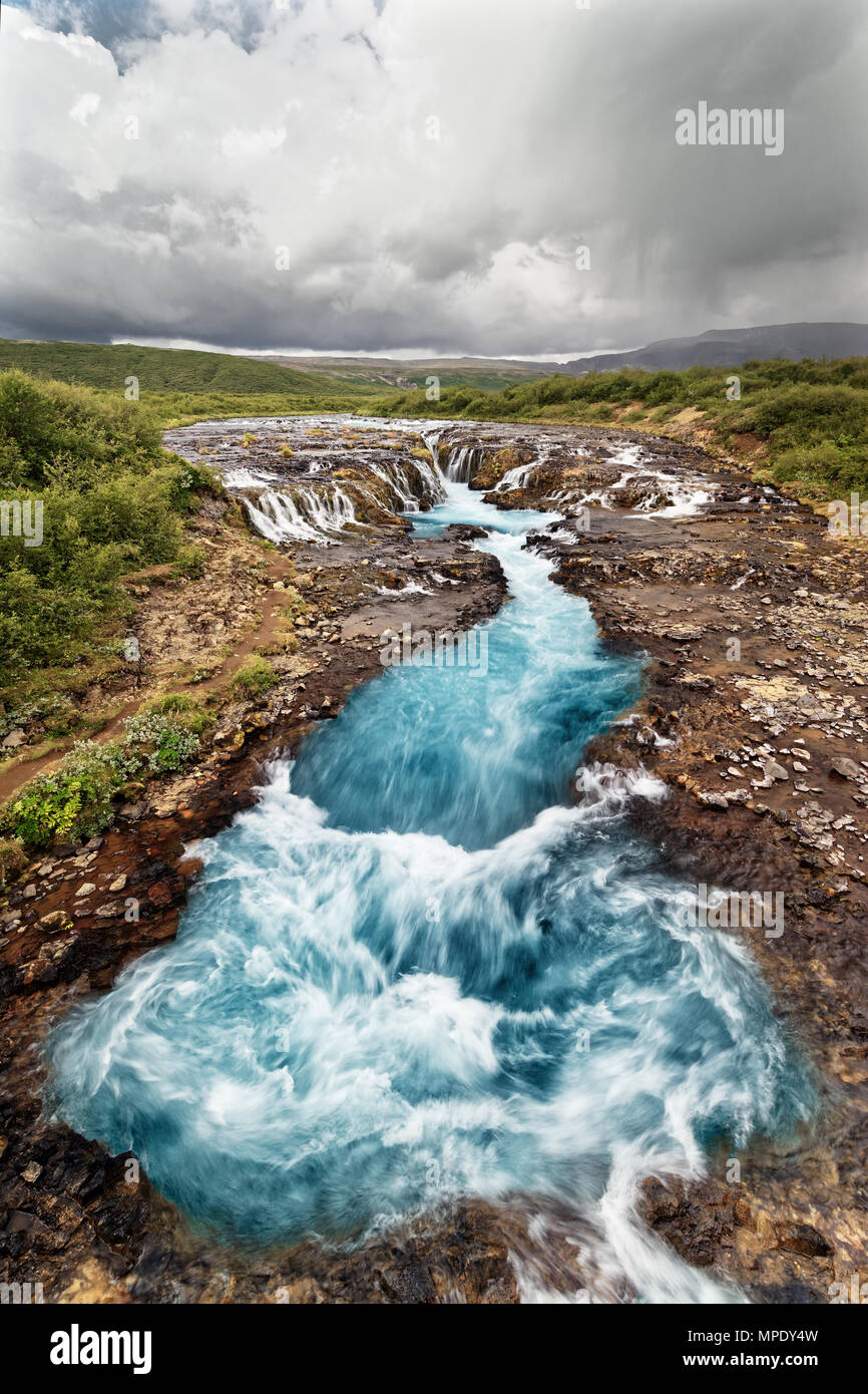 Scenic view of a waterfall with blue coloring, in the background a mountain range - Location: Iceland, Golden circle Stock Photo