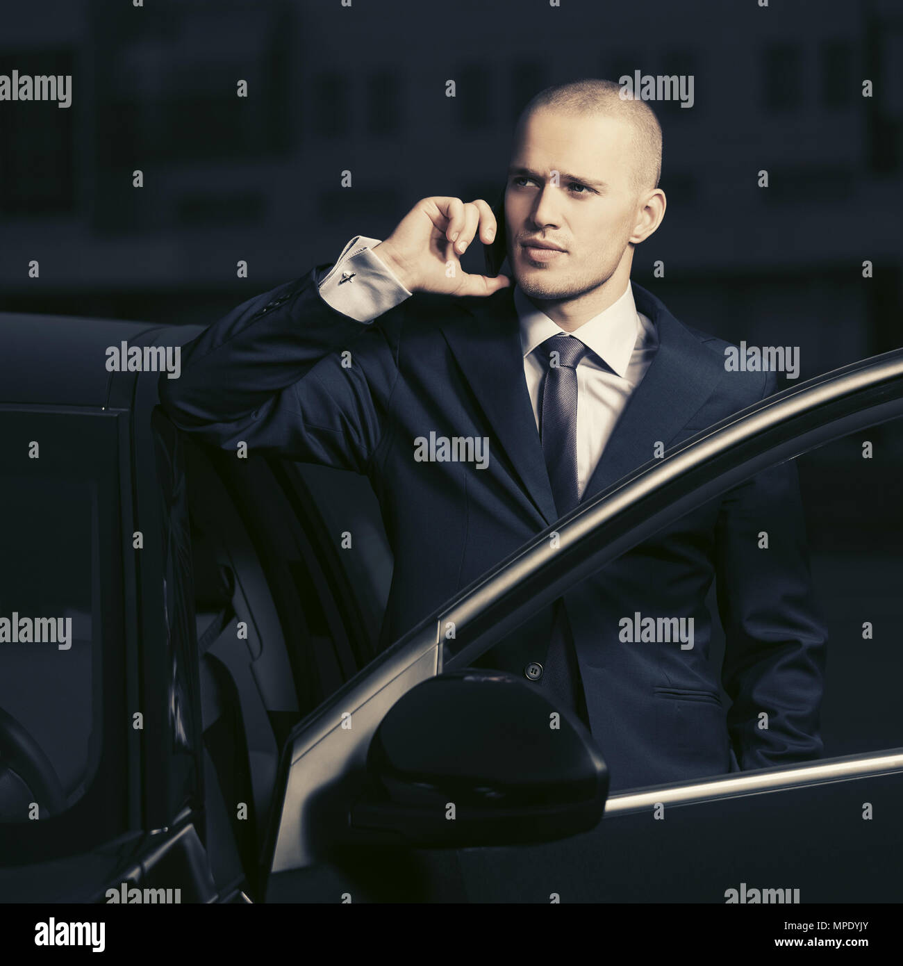Young businessman in dark blue suit calling on cell phone outside a his car Stock Photo