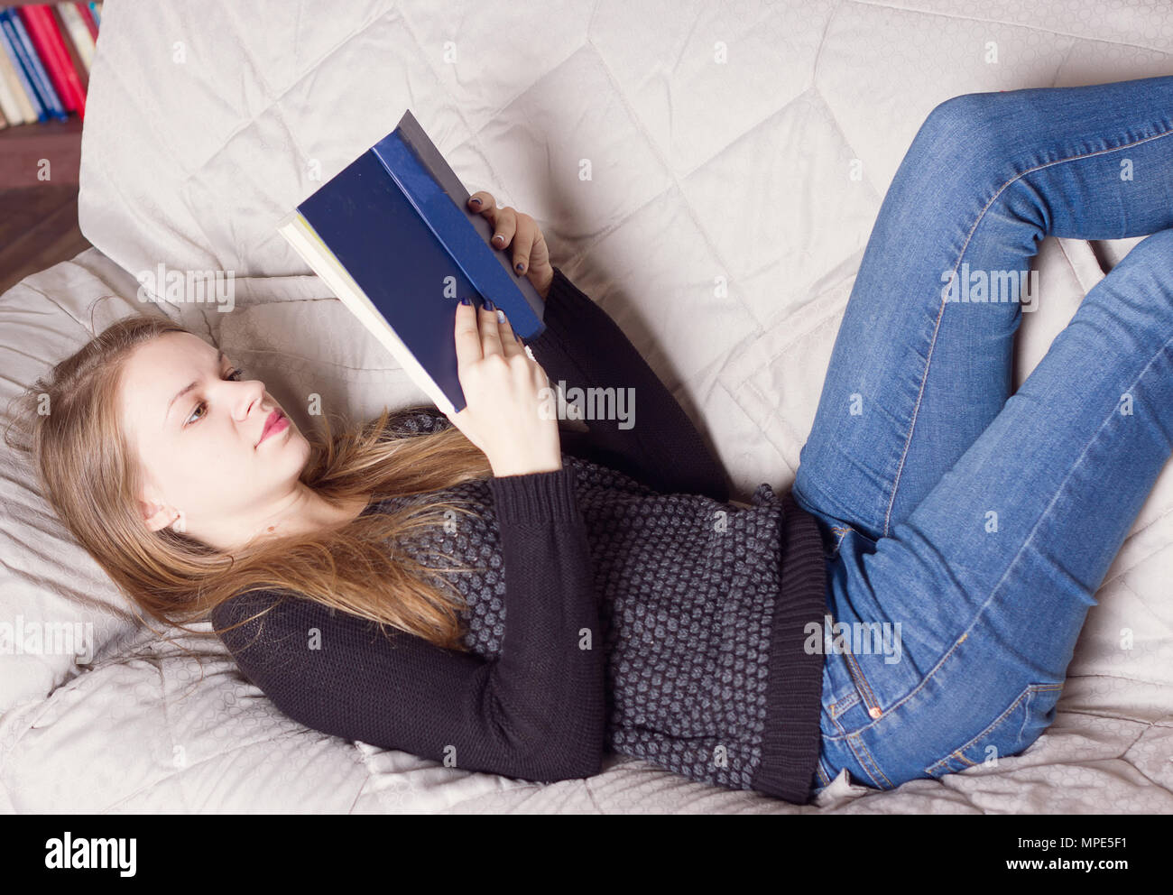 Beautiful young blond woman reading book on the bed at home Stock Photo