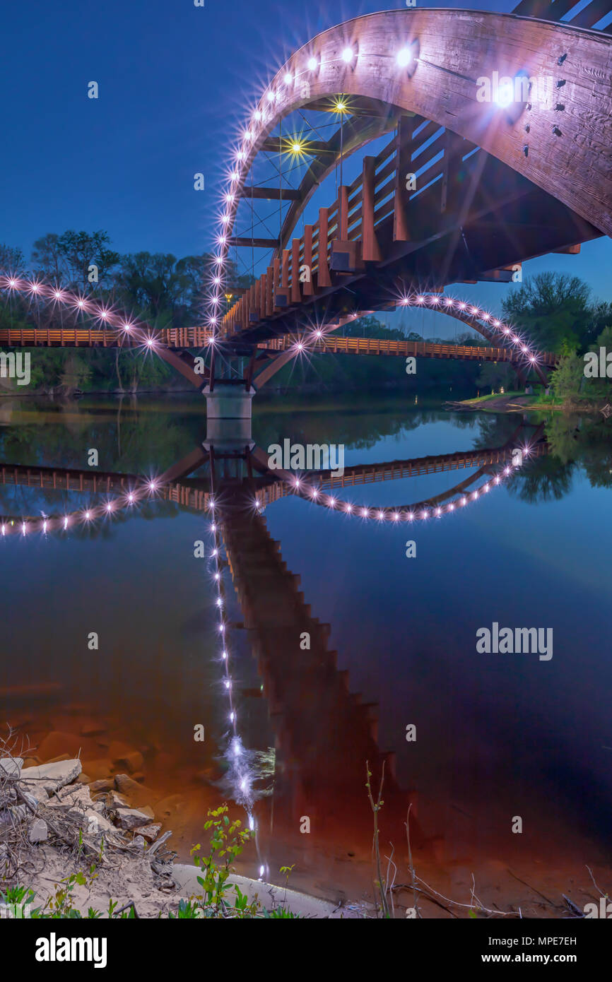 The Tridge at night, spans the confluence of the Chippewa and Tittabawassee Rivers in Chippewassee Park in Midland, Michigan. The bridge reflects in t Stock Photo