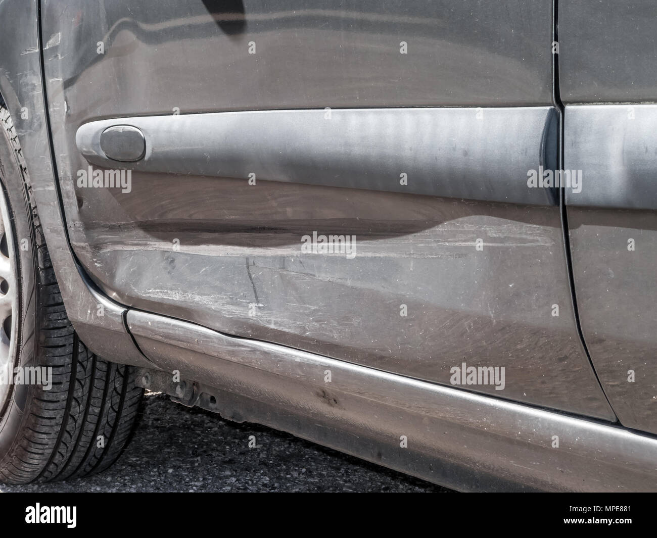Close up detail of a dented driver door from a car crash or automobile accident. Bent and distorted metal with large dent and body paint scratched Stock Photo