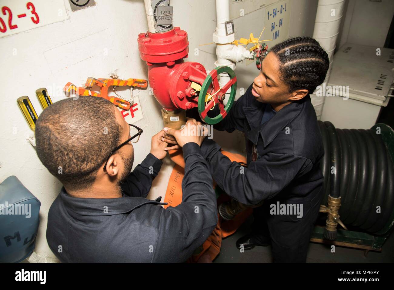 170209-N-KJ380-019  ATLANTIC OCEAN (Feb. 9, 2017) Aviation Ordnanceman Airman Levi Turner, left, from Atlanta, and Airman Yasmene Harris, from New York, attach a hose to a aqueous film-forming foam cut-out valve in the Aircraft Intermediate Maintenance Department tunnel aboard the aircraft carrier USS Dwight D. Eisenhower (CVN 69) (Ike). Ike is currently conducting aircraft carrier qualifications during the sustainment phase of the Optimized Fleet Response Plan (OFRP). (U.S. Navy photo by Mass Communication Specialist Seaman Neo Greene III) Stock Photo