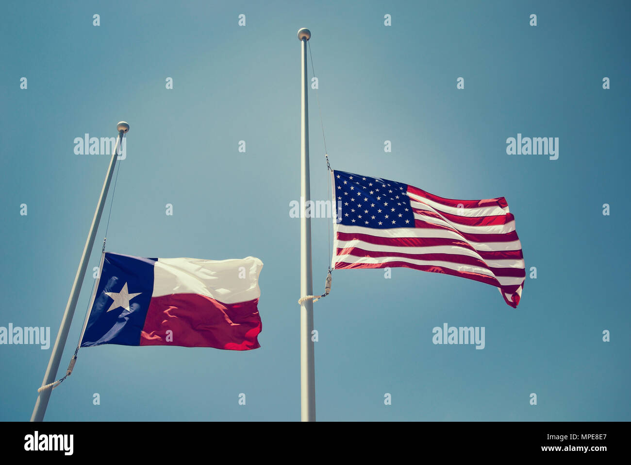 The state flag of Texas and the United States flag flying at halfmast