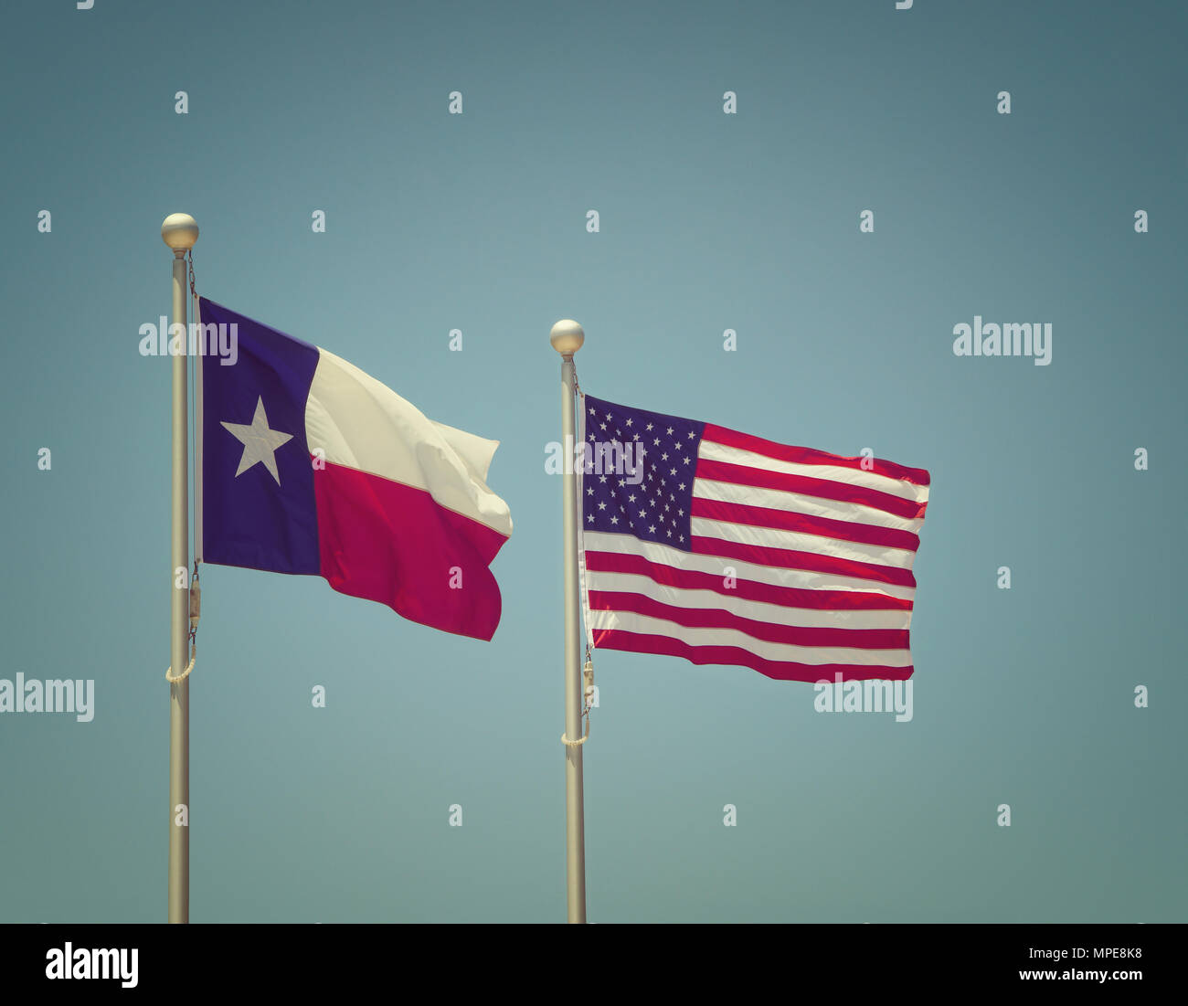 The state flag of Texas and American flag waving in the wind on flagpole. Blue sky background with copy space. Vintage filter effects. Stock Photo