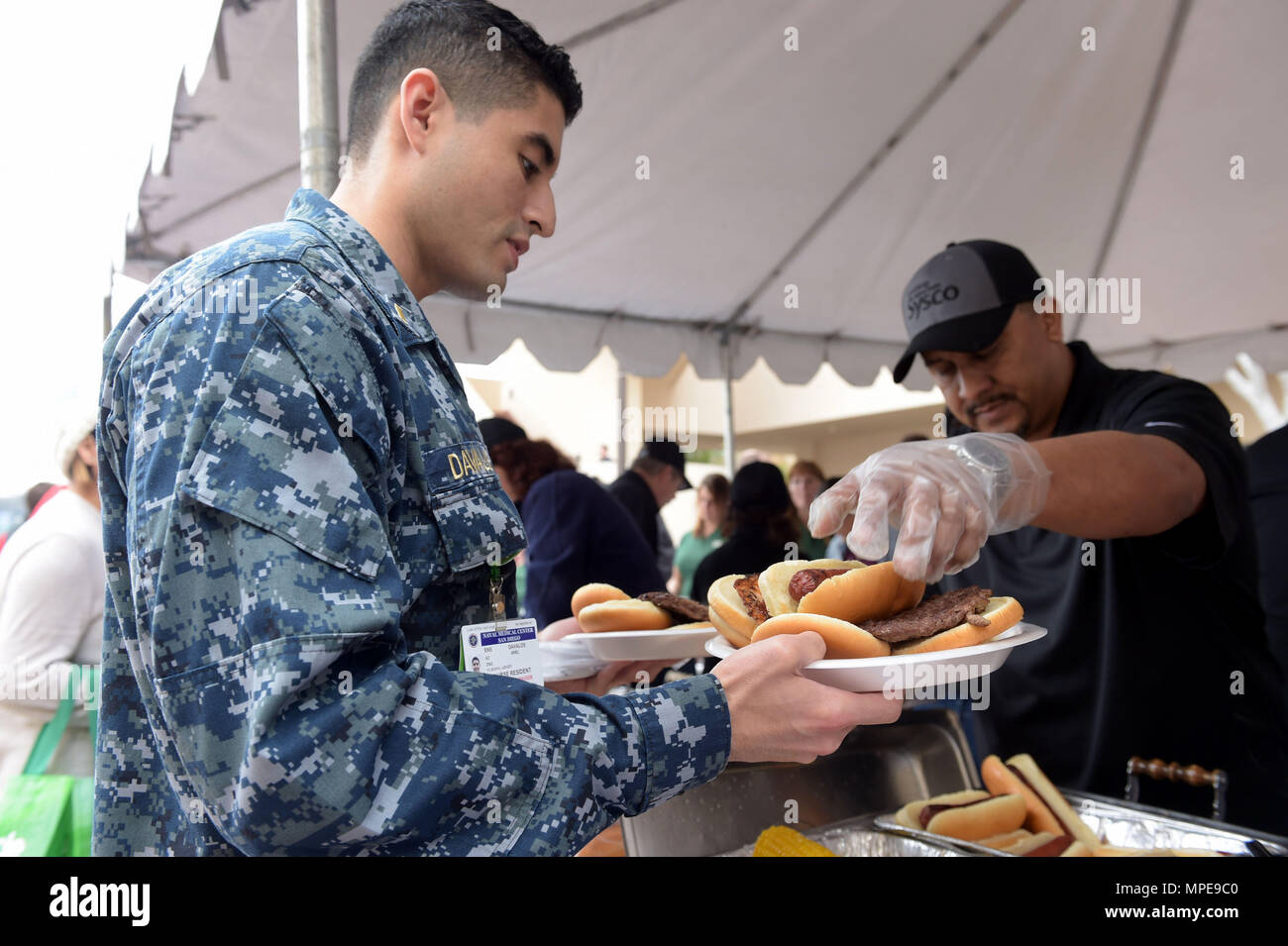 170211-N-WR119-045 SAN DIEGO (February 11, 2017) Ensign Ariel Davalos gathers food for his Sailors from a Sysco food services volunteer during the Invincible Spirit Festival put on by the Gary Sinise Foundation at Naval Medical Center San Diego. The festival featured a live performance by Gary Sinise and the Lt Dan Band, show and shine car show, cookout by celebrity chef Robert Irvine, and many more family activities. The Gary Sinise Foundation serves our nation by honoring our defenders, veterans, first responders, their families, and those in need. (U.S. Navy photo by Mass Communication Spec Stock Photo