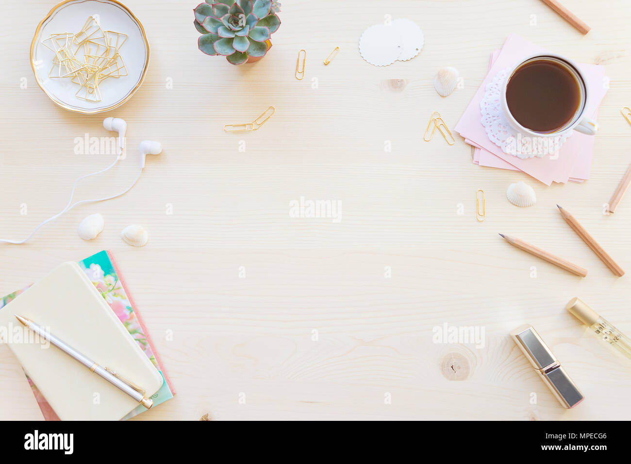 Female home office desk table in pastel tones. Workspace with notebooks, cup of coffe and decorations on light wooden background with copy-space. Flat Stock Photo