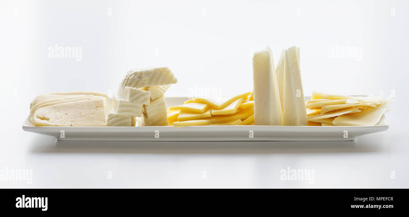 Rectangular white porcelain plate, filled with pieces of cheese of different varieties. Side view Stock Photo