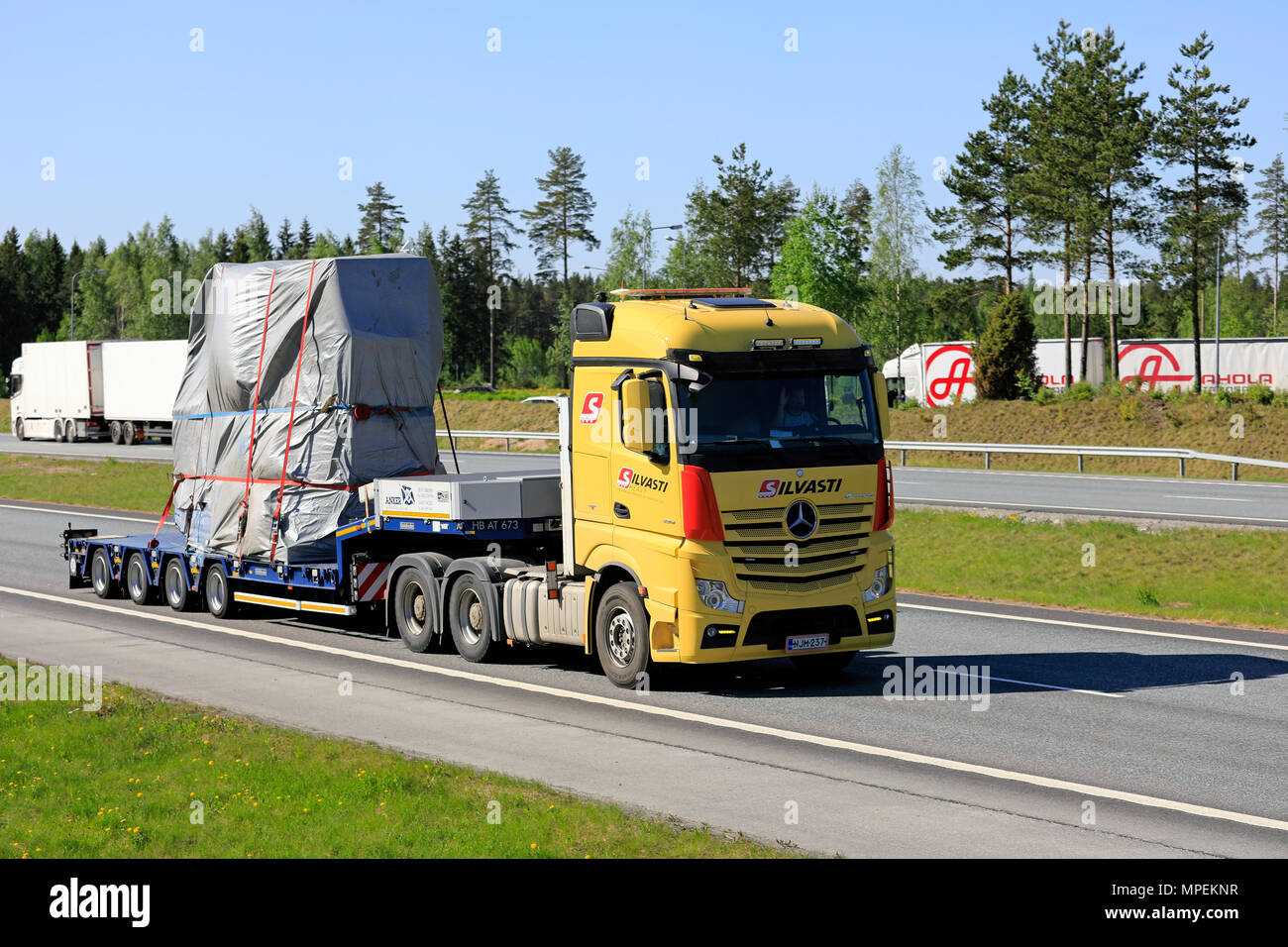 Yellow Mercedes-Benz Actros 3351 semi trailer of Silvasti Heavy transports industrial object on motorway in the summer. Other trucks on the background Stock Photo