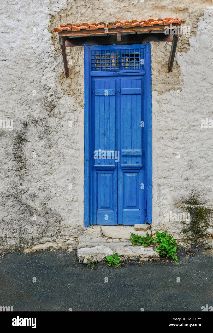 Old building with interesting blue wooden doors that are closed.  Vibrant blue in colour and a grill pattern at the top, covered by a tiny tiled roof. Stock Photo