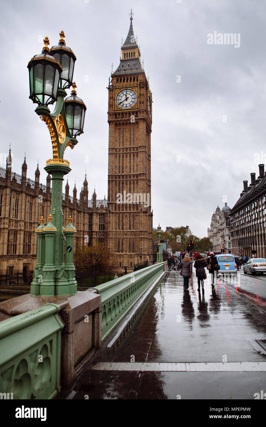 People walk on the Westminster Bridge over the Thames River near Parliament on a cloudy late afternoon. Stock Photo