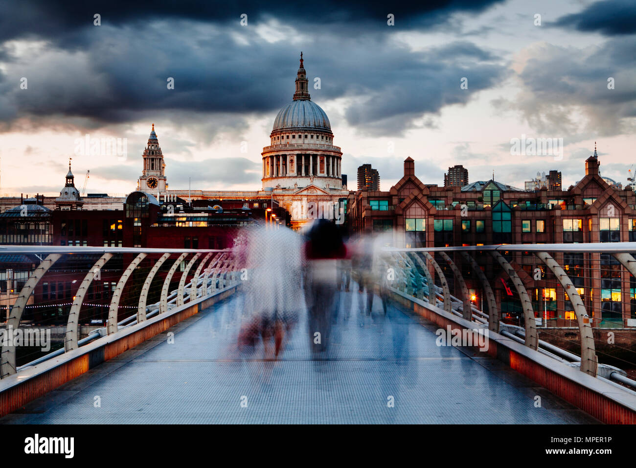 Early evening on London's Millennium Bridge with people crossing in motion blur and a view of St Pauls Cathedral. Stock Photo